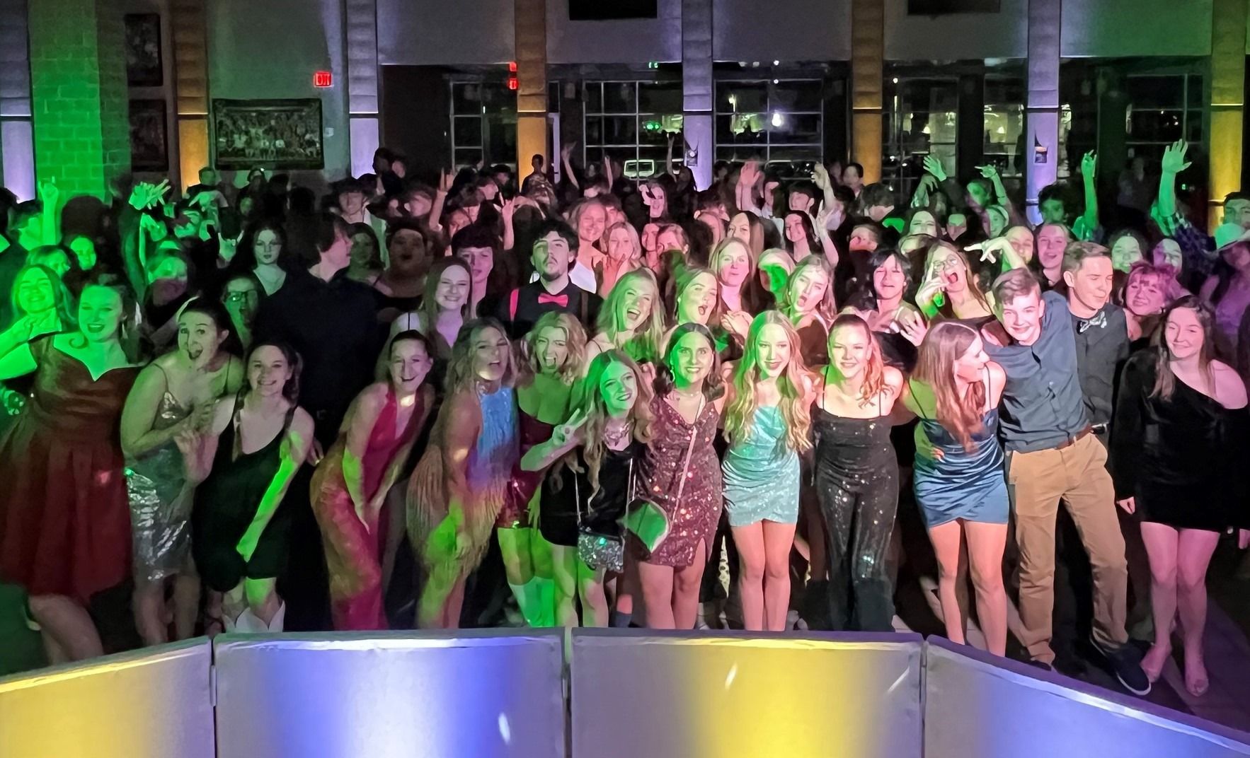 Large group posing on a dance floor under green and pink lights, smiling at a party event.
