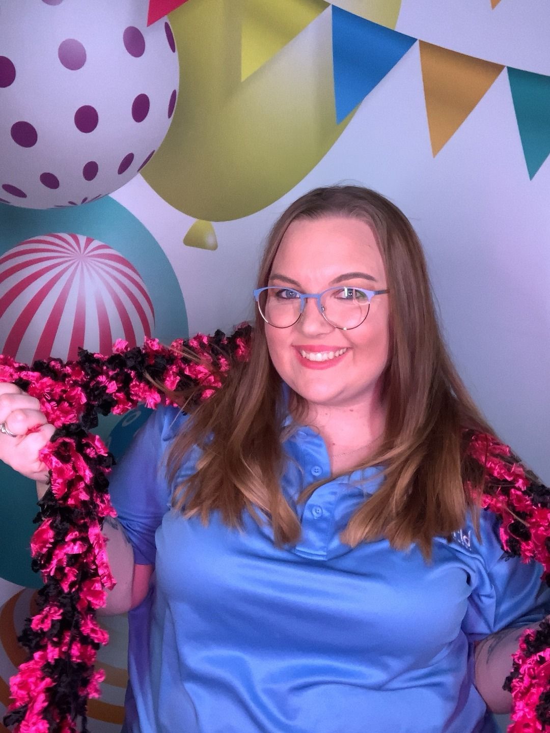 Smiling woman in a blue satin top at a colorful birthday-themed backdrop