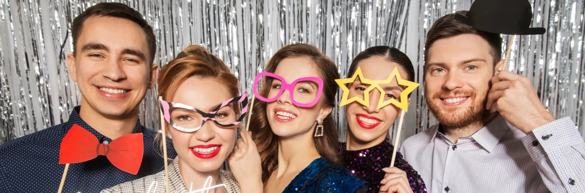 Five friends smiling and posing with colorful party glasses and bow ties at a celebration