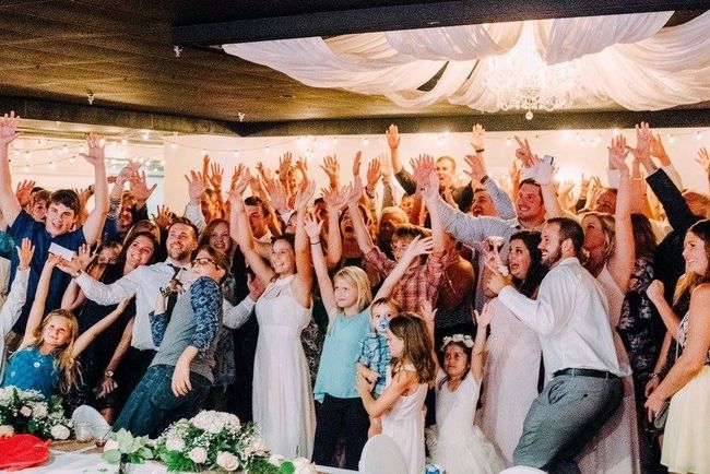 Crowd dancing and cheering at a lively indoor celebration with raised hands and colorful decor