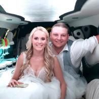 Couple in wedding attire sitting in a limo, smiling at the camera.
