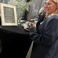 Woman standing beside a black table with a framed sign at an indoor event.