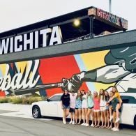 Group posing by a white limo in front of a Wichita baseball mural.