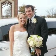 Bride and groom smiling beside a white limousine, holding a bouquet outdoors