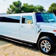 White stretch limousine parked outdoors on gravel with trees in the background.