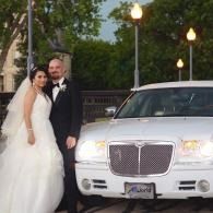 Bride and groom posing beside a white luxury car at dusk
