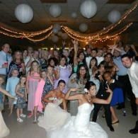 Wedding reception with bride and groom posing with a large group of smiling guests under hanging lights