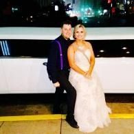 Two people posing together at night by a white limo, wearing dark and light formal outfits.