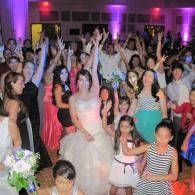 Crowded wedding reception with guests dancing under purple lights, bride in a white gown near center