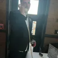 Man in black suit talking on a phone beside a table in a dimly lit room