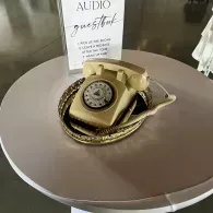 Vintage beige rotary telephone displayed on a round table with a small sign behind it.