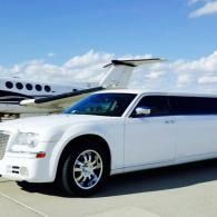 White stretch limousine on an airport tarmac with a private jet in the background