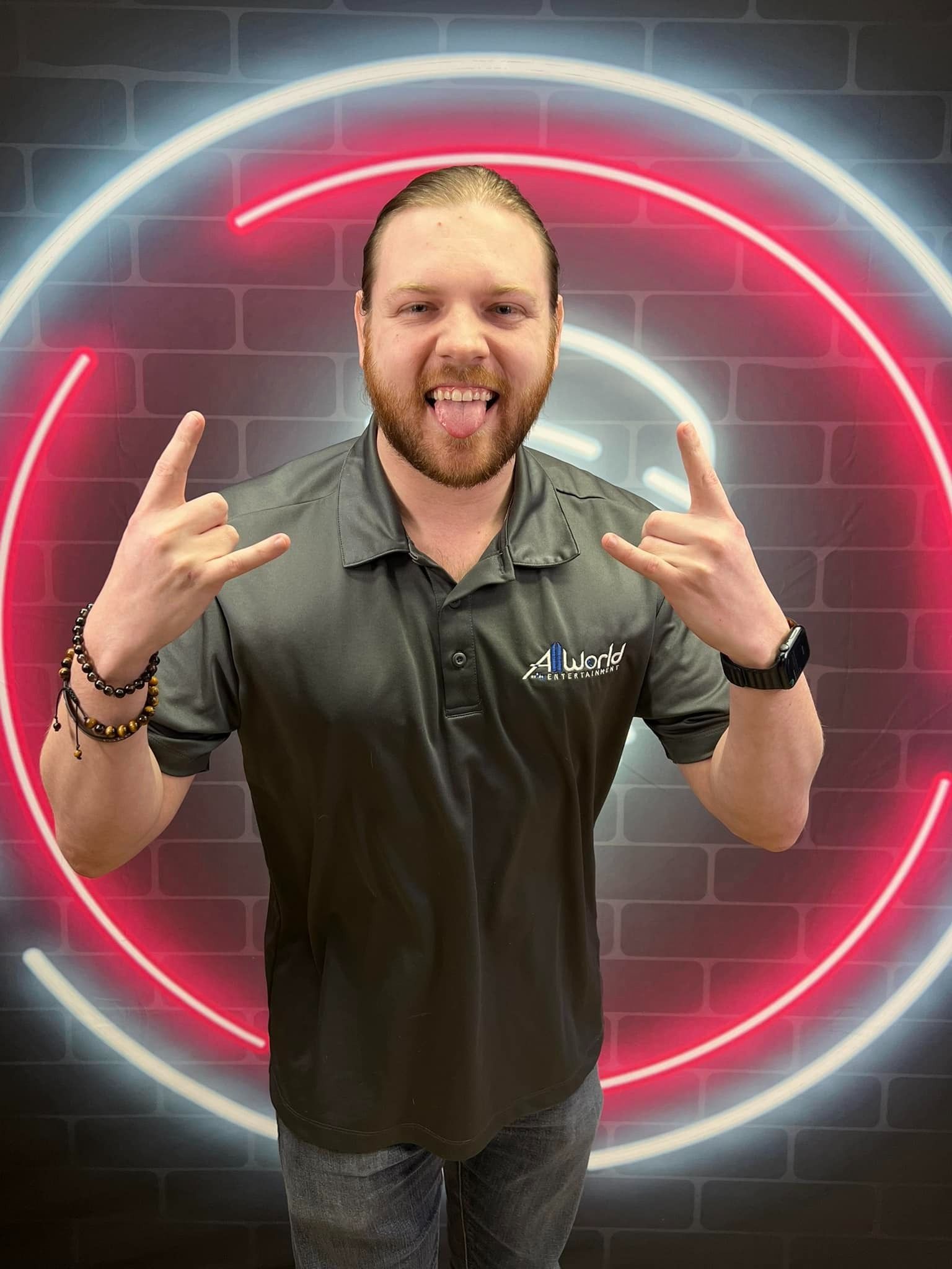 Man standing in front of a neon red circle, smiling and making rock hand signs.