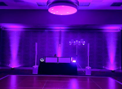 Purple-lit banquet hall with a decorated DJ table and uplighting on brick walls