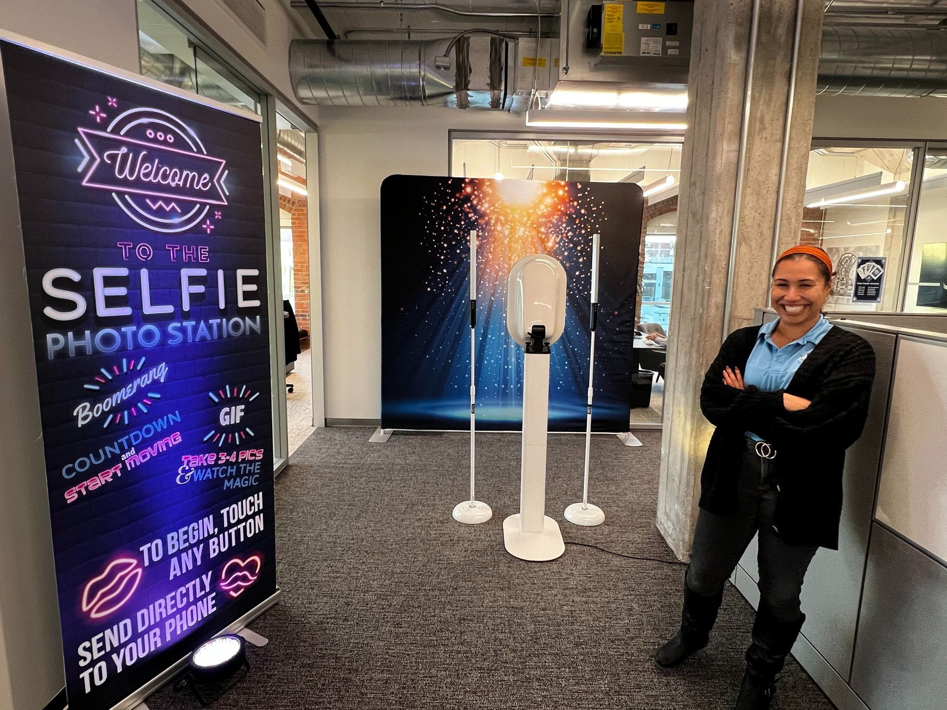 Indoor selfie station with a smiling person beside a glowing light display and phone stand