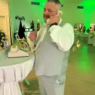 Man in a light gray suit talking on a phone at a decorated indoor event reception