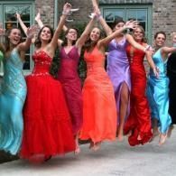 Women in colorful formal dresses dancing outdoors, arms raised and smiling