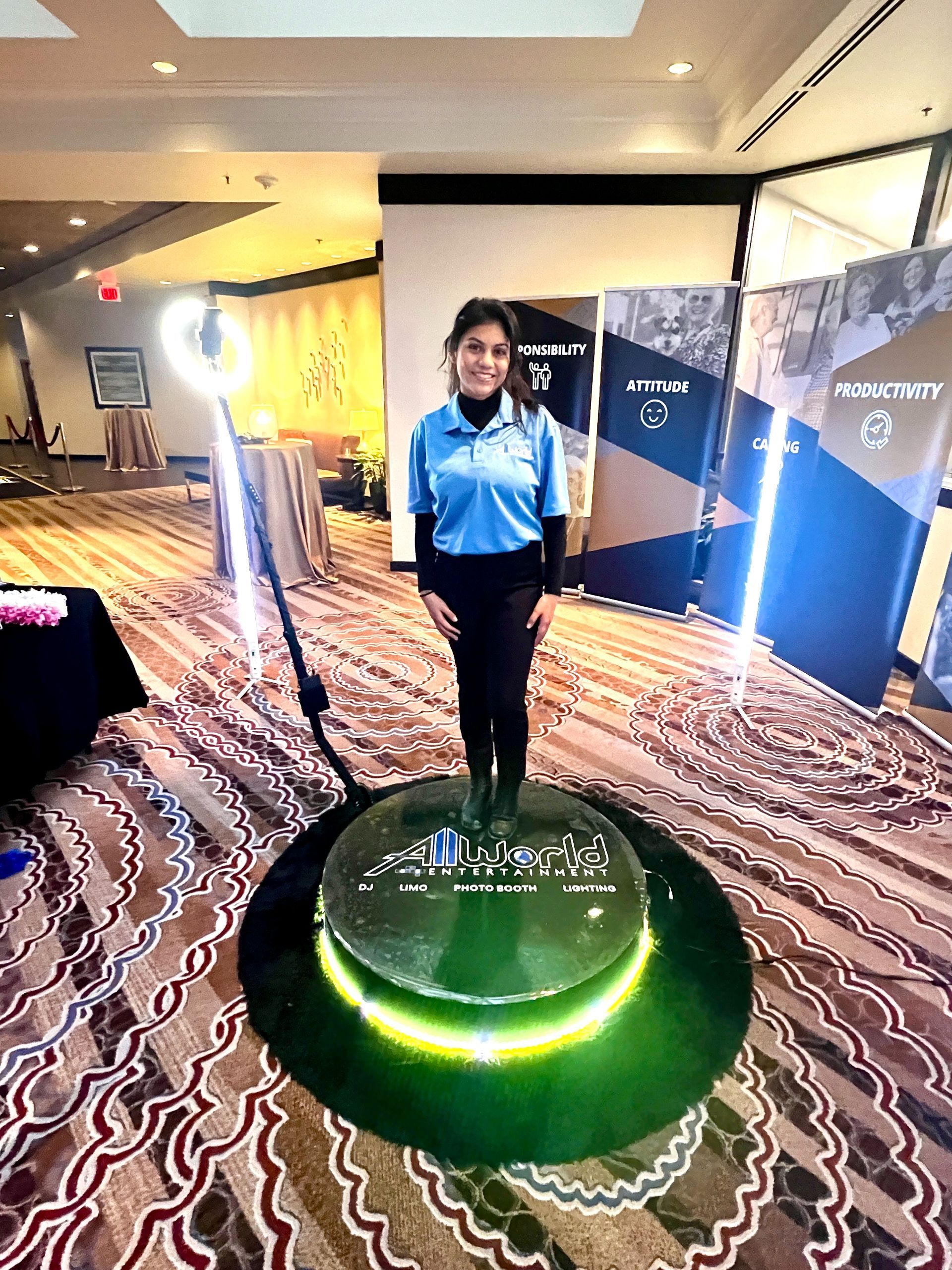 Woman in blue uniform standing beside a glowing green display in a conference hall