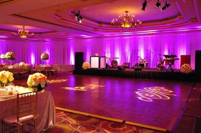 Empty banquet hall lit in purple, with chandeliers, dance floor, and stage at the far end