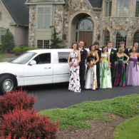 Group of people in formal dresses standing by a white limousine in front of a large house