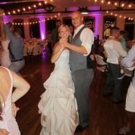 Bride and groom slow dancing at a wedding reception with purple uplighting and guests nearby
