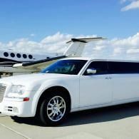 White stretched limousine parked on an airport tarmac beside a private jet under a blue sky