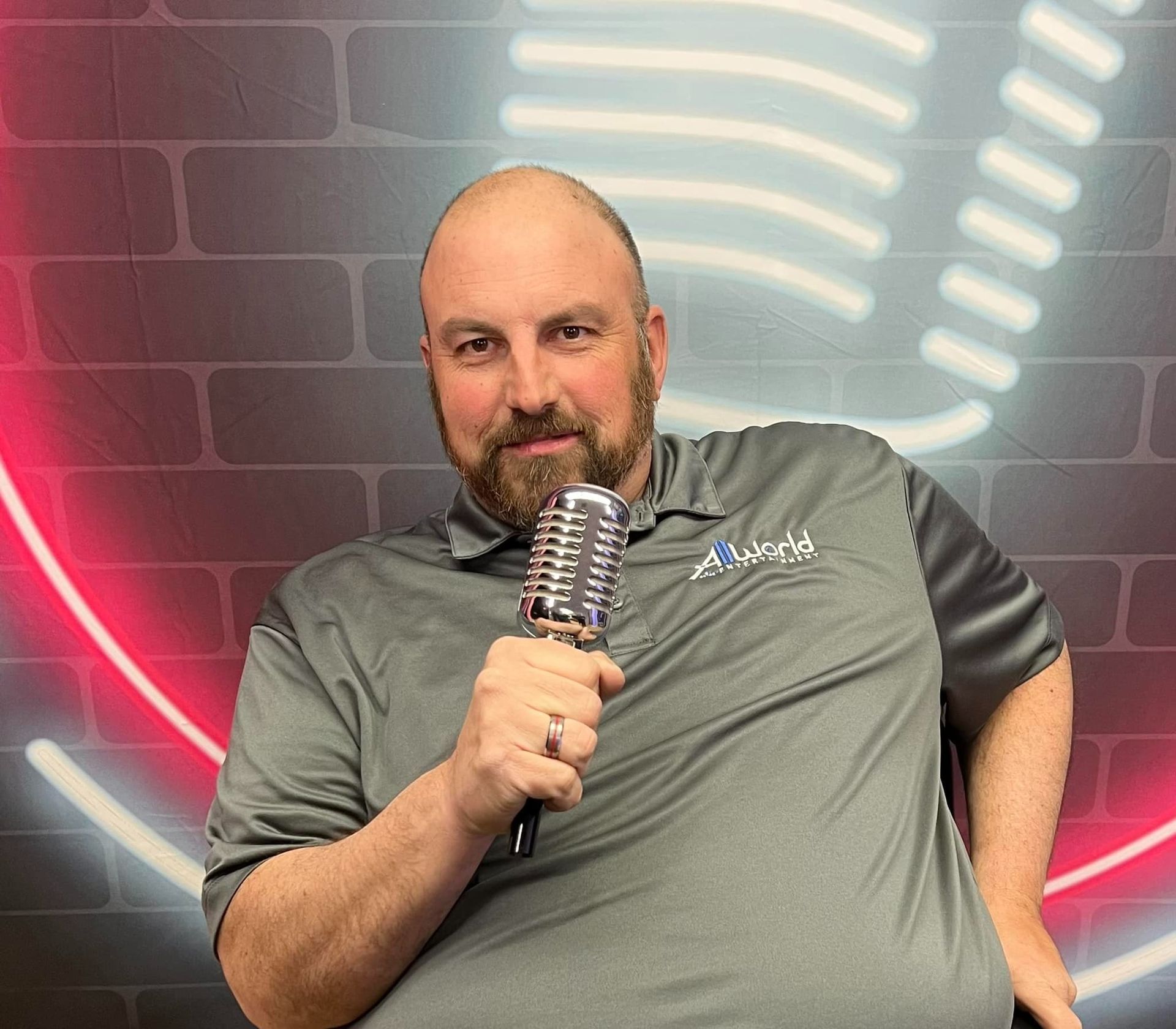 Man holding a microphone in front of a brick wall with red and white neon lights