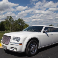 White luxury limo parked outdoors on a sunny day under a partly cloudy sky.