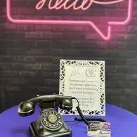 Vintage black rotary phone on a purple table beneath a pink neon 