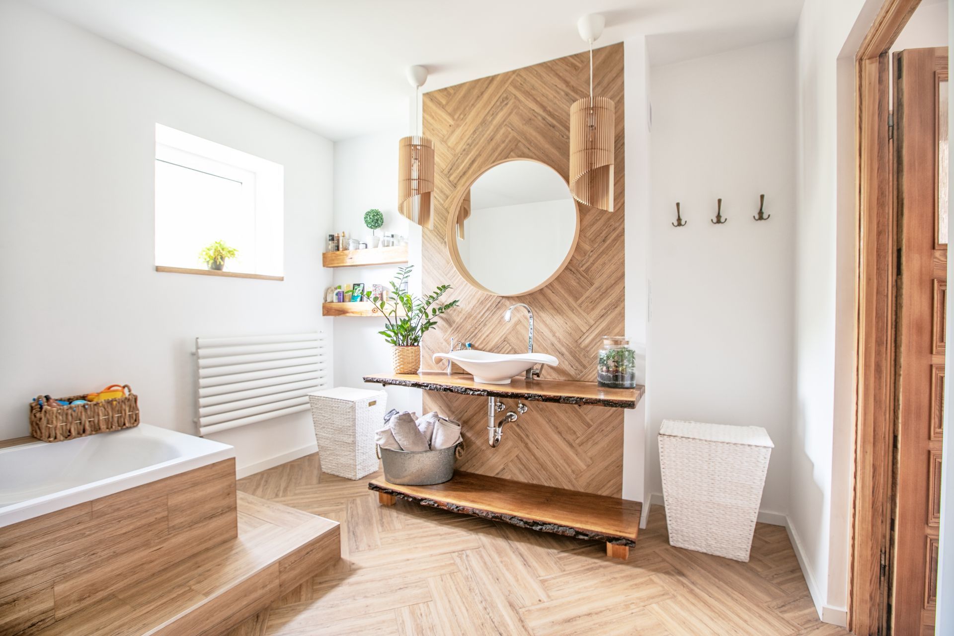 Bright modern bathroom with wood vanity, round mirror, and herringbone floor, in soft neutral tones