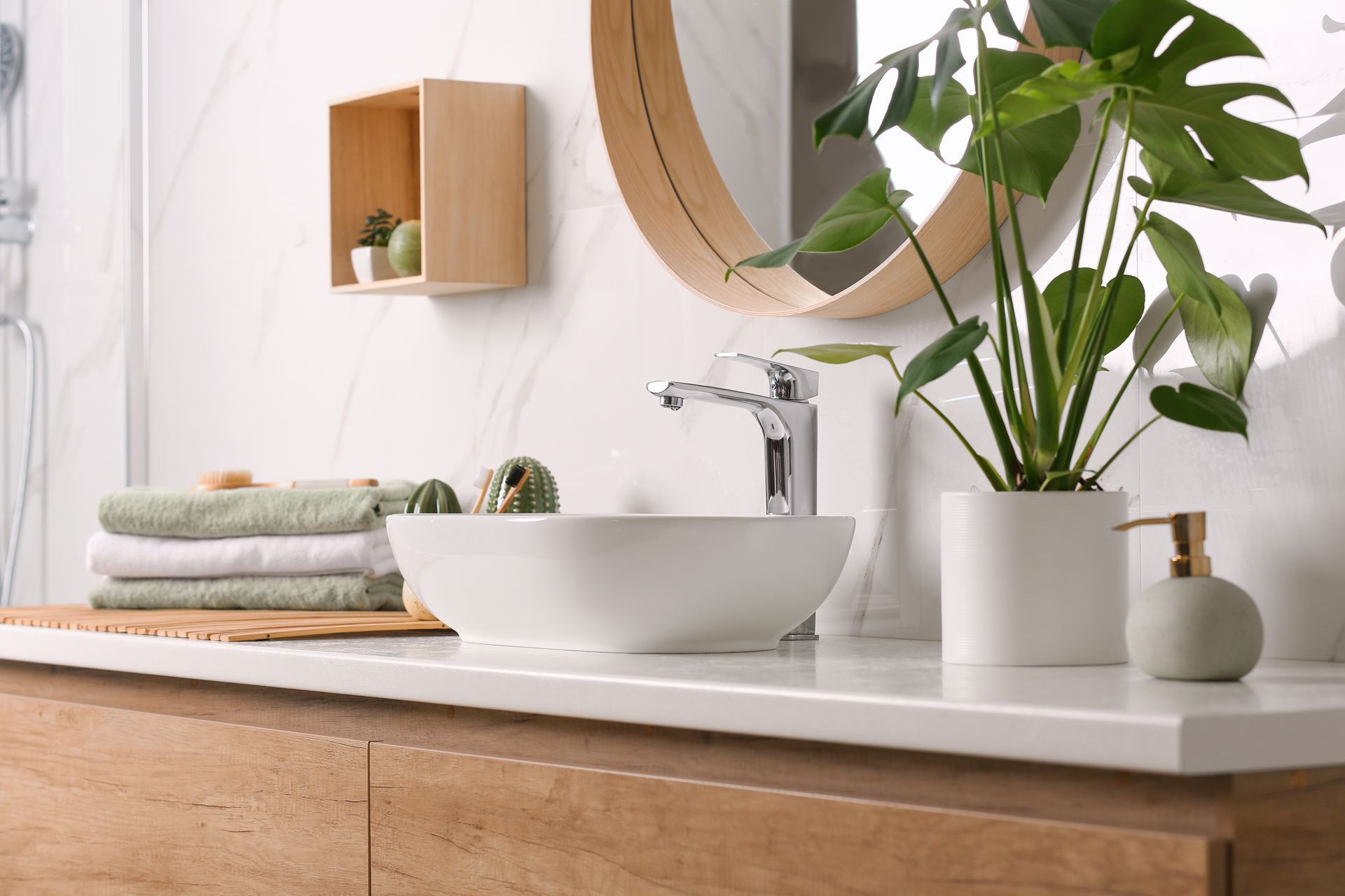 Modern bathroom vanity with white sink, wood countertop, round mirror, towels, and green plant
