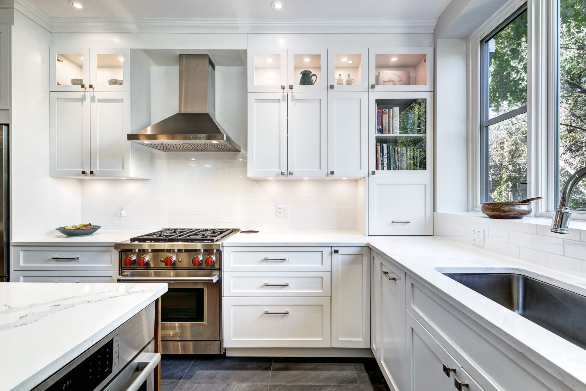 Bright white modern kitchen with stainless steel stove, hood, and large windows
