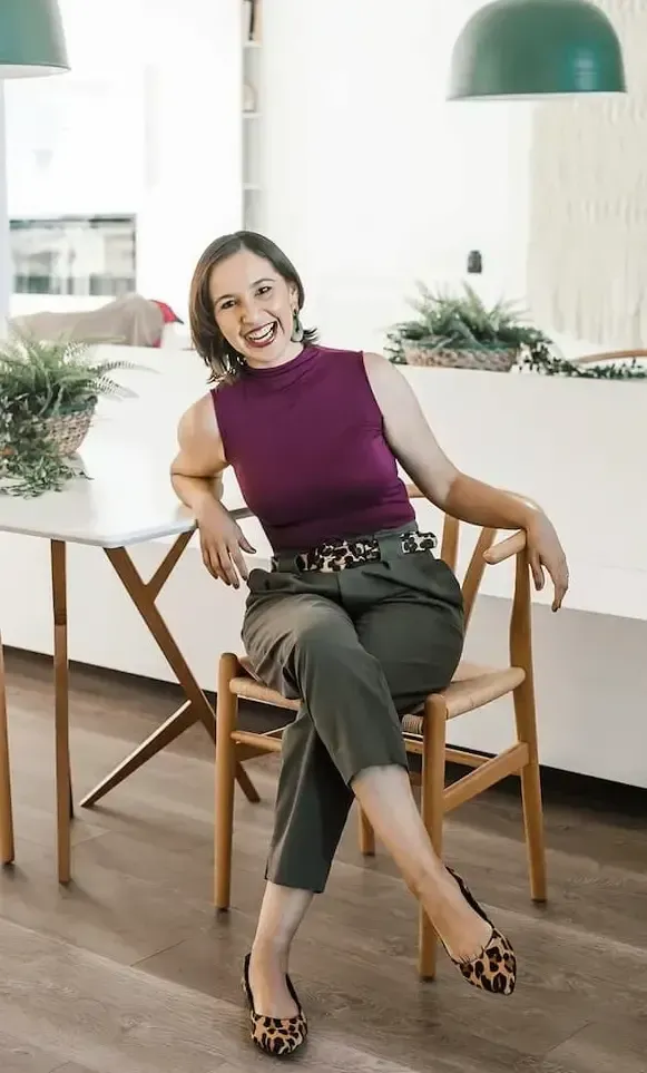 A woman is smiling in front of a brick wall.