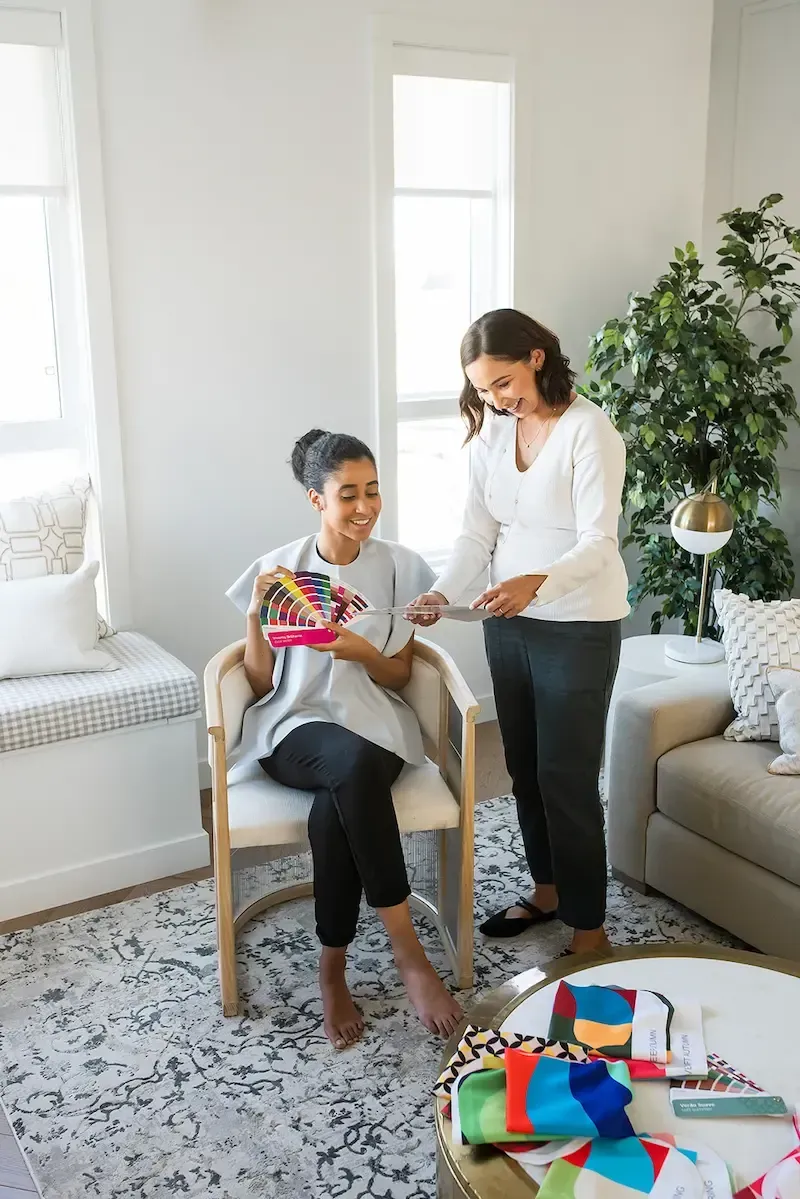 Two women are looking at a color palette in a living room.