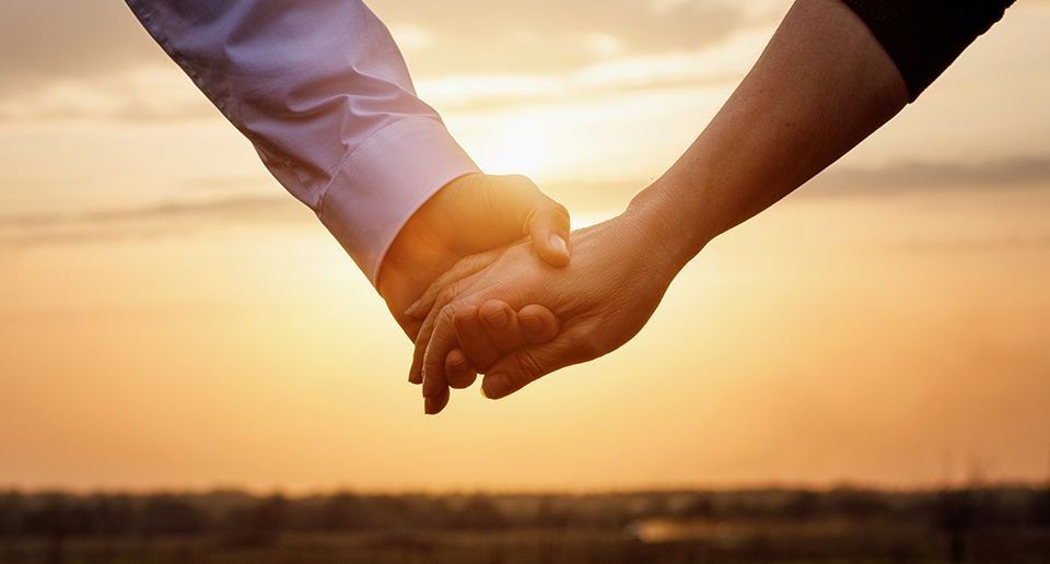 Two people holding hands across a wooden table, offering comfort and support.