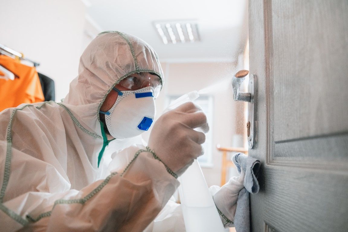 Person in protective suit cleaning a bathroom surface with a spray bottle