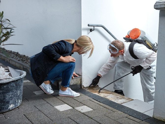 Two workers in protective gear inspect damage on a rooftop beside a crouching woman