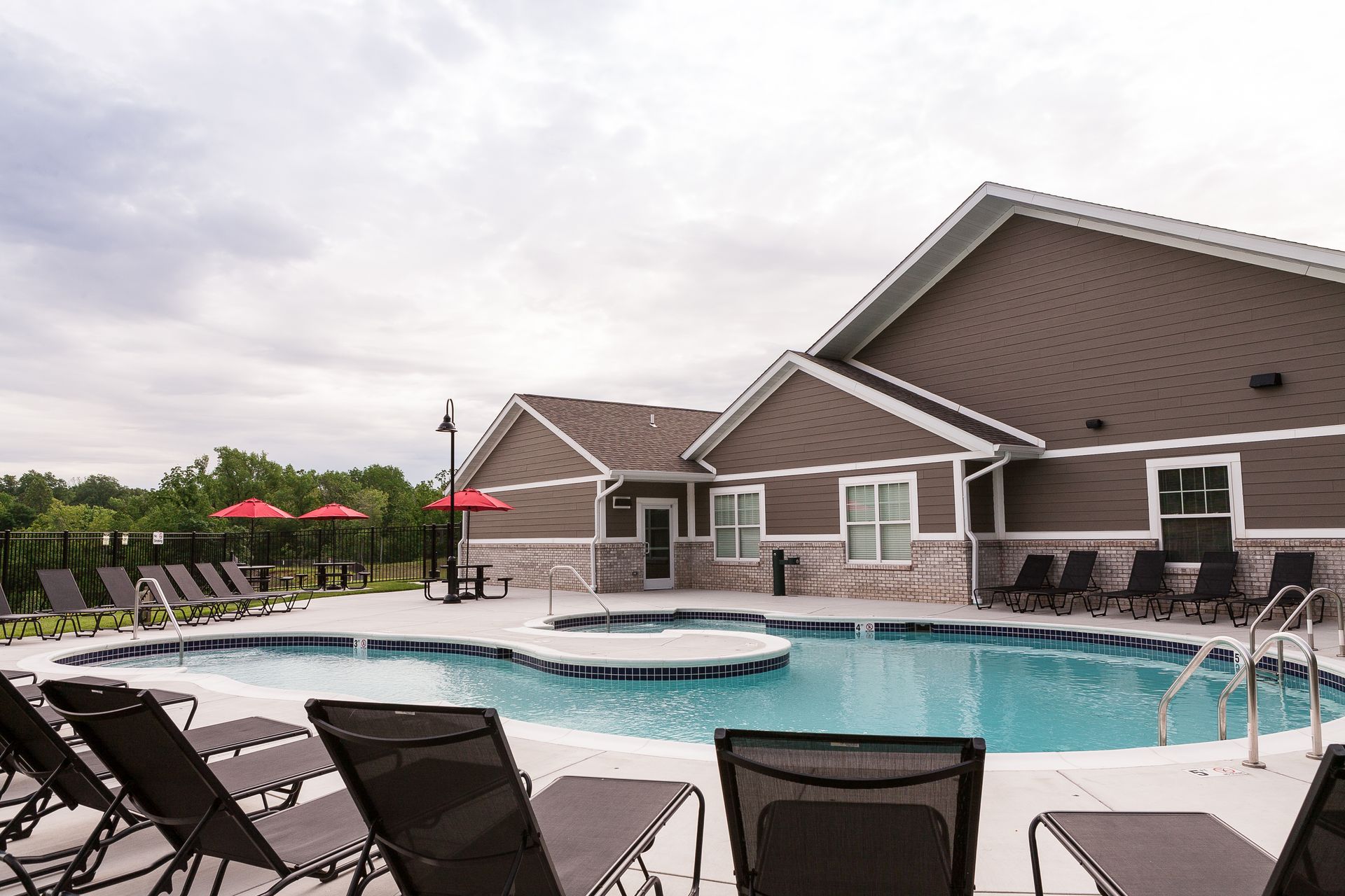 a large swimming pool surrounded by chairs and umbrellas in front of a house .