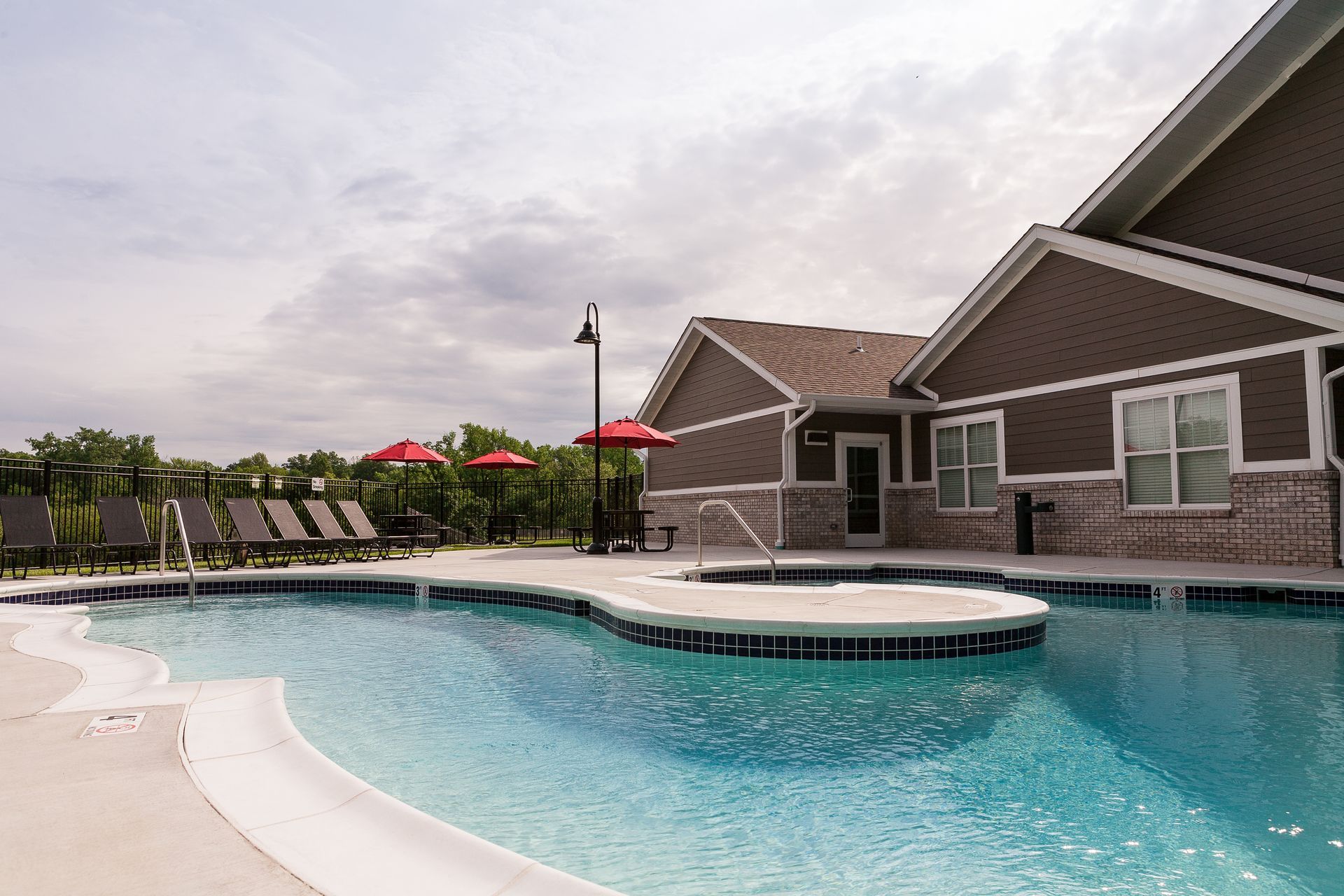 a large swimming pool is surrounded by chairs and umbrellas in front of a house .