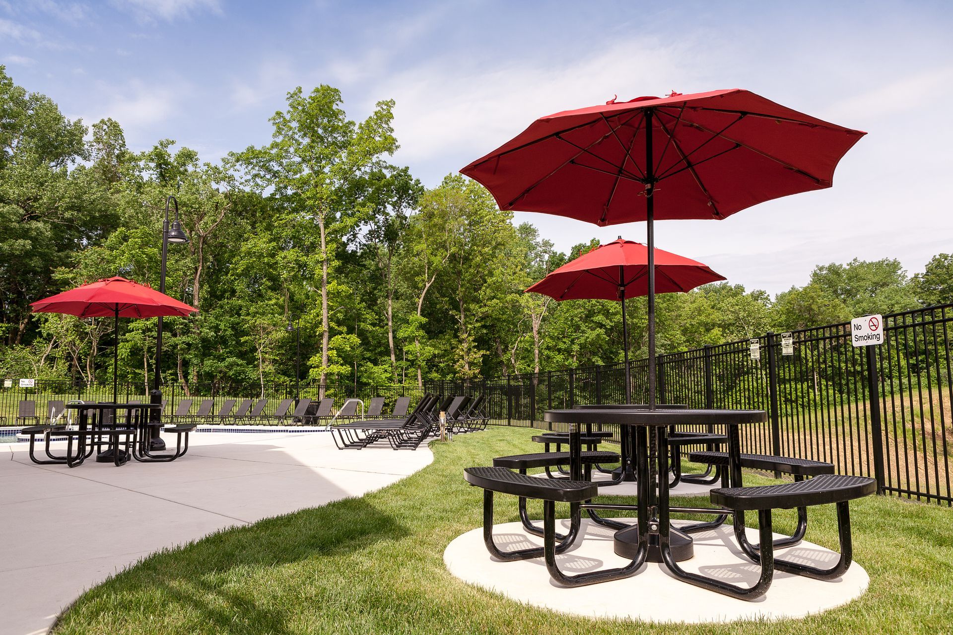 a picnic table with two red umbrellas in front of a pool .