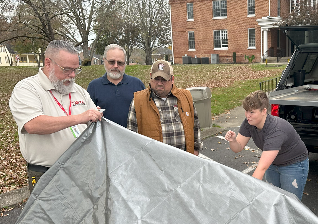 Macy participating in early response training with the United Methodist Committee on Relief on Union's campus. Together, they are working with a gray tarp.