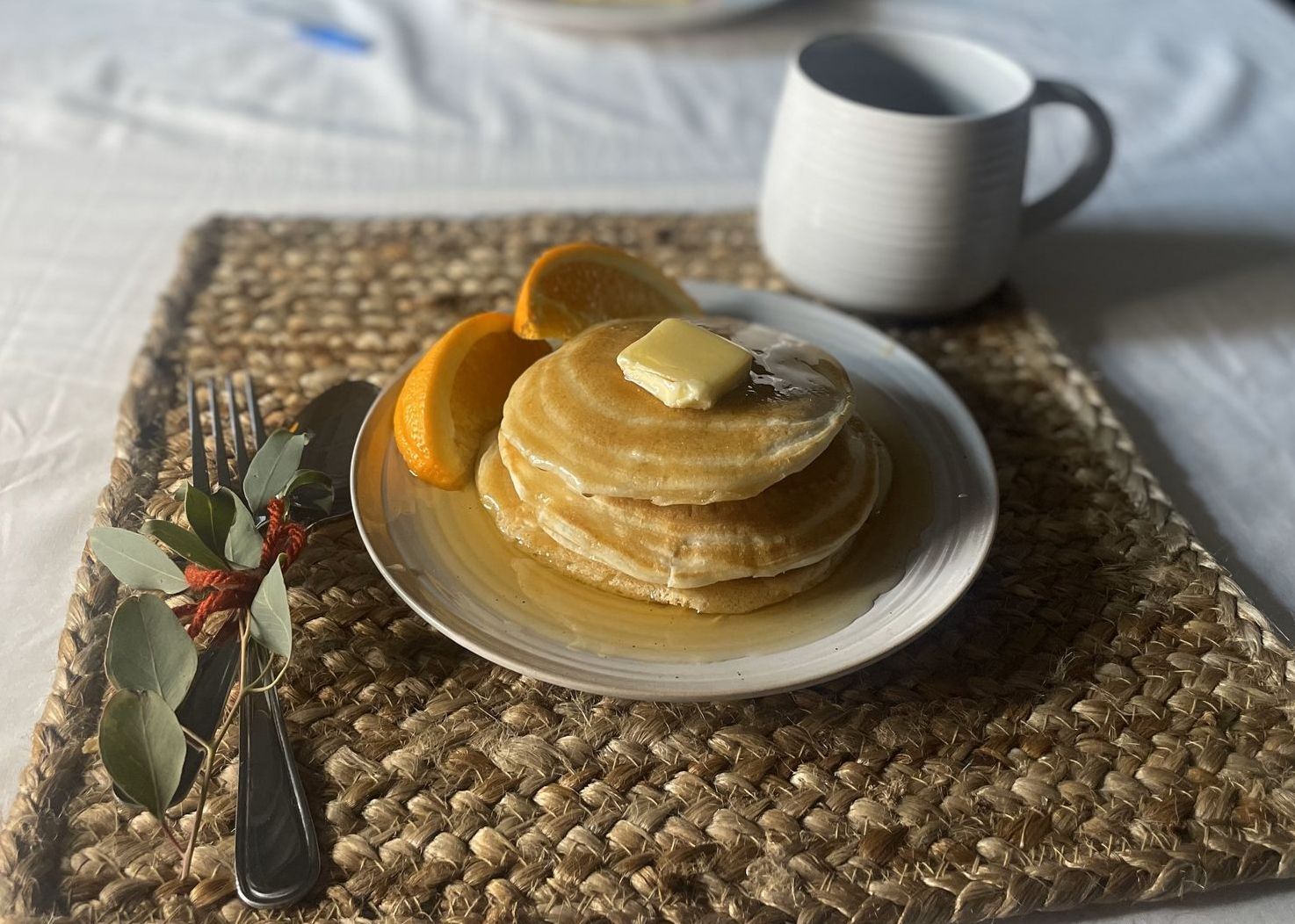 An inedible yet delicious looking plate of pancakes and oranges sits on a woven tray with a fork and a coffee cup.