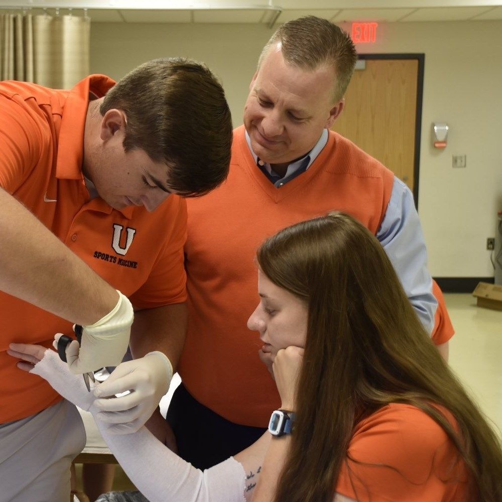 Dr. Douglas Branch observes two students studying athletic training practice their casting techniques during a hands-on class.