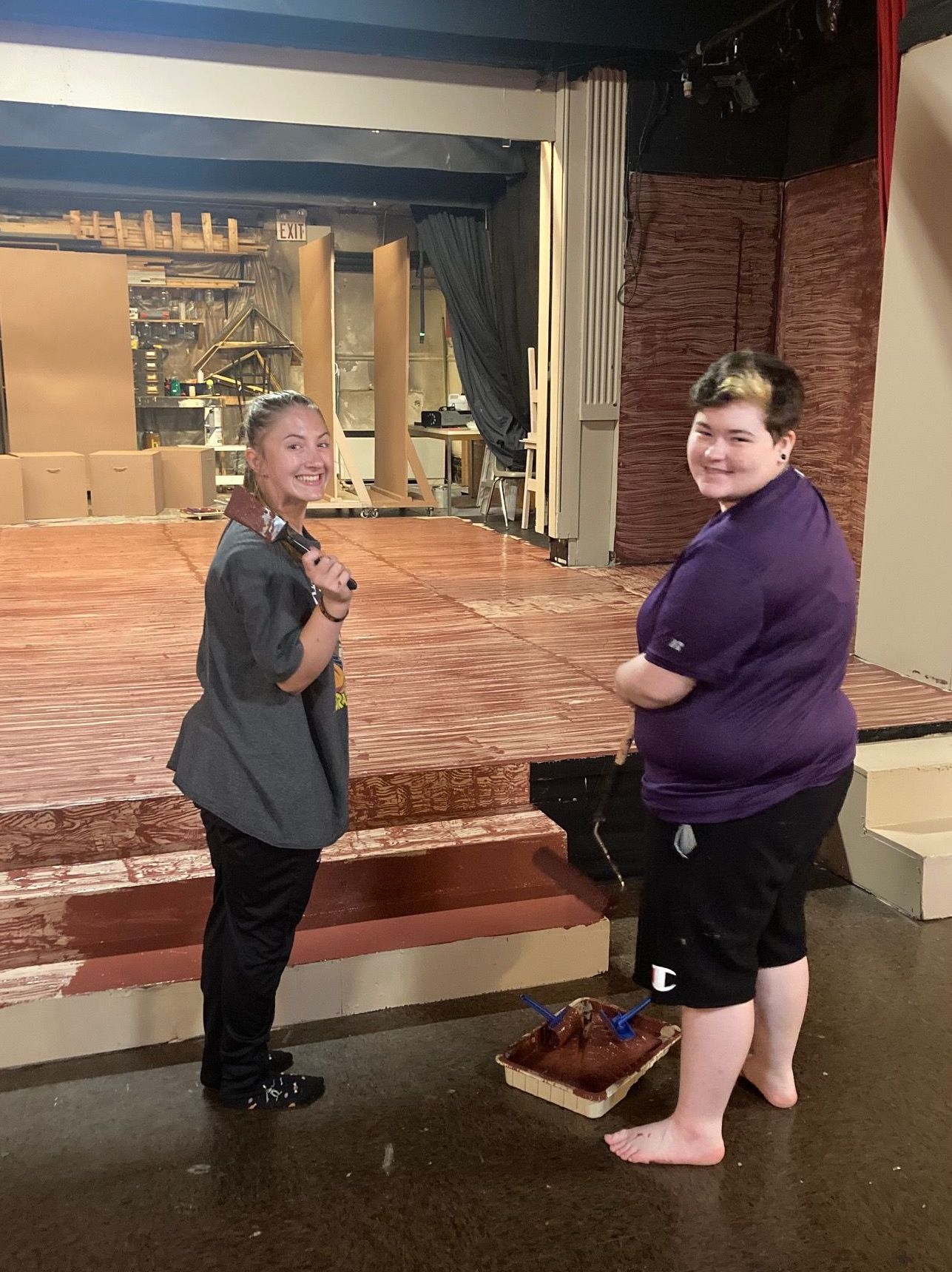 Erin and Conner standing at the set of An Unspeakable Triumph of Supreme Brilliance holding paintbrushes soaked in brown paint.