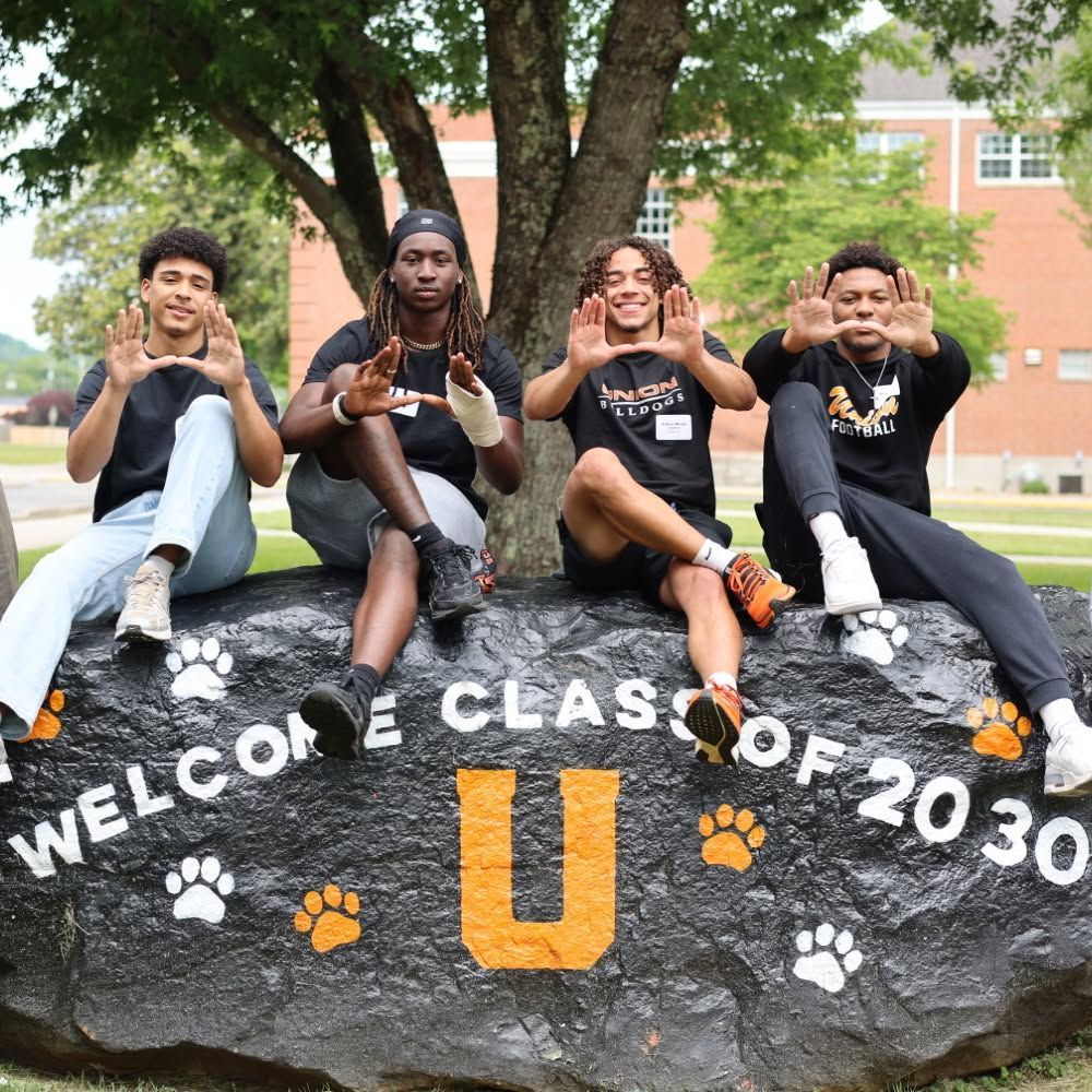 4 students sitting on top of the campus spirit rock making a 