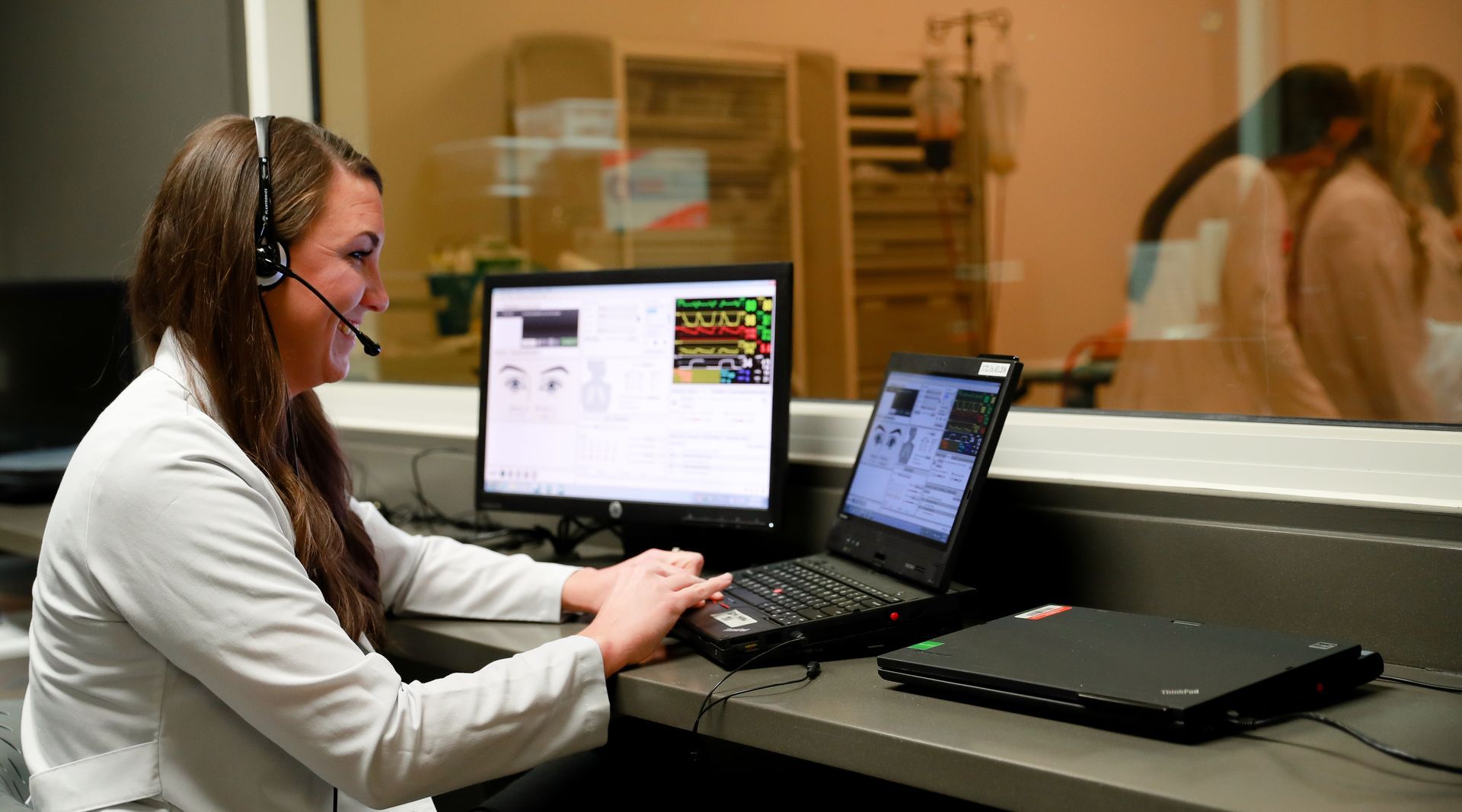 Professor Amanda Hensley working with telesimulation technology including a laptop, monitor, and headset.