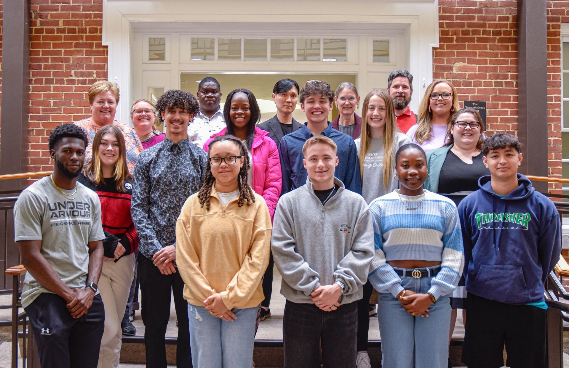 Student awardees stand with grant committee members and advisors behind them in the center of the Sharp Academic Center's atrium.