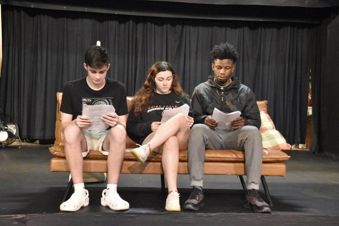 Actors sitting on a couch reading their scripts.