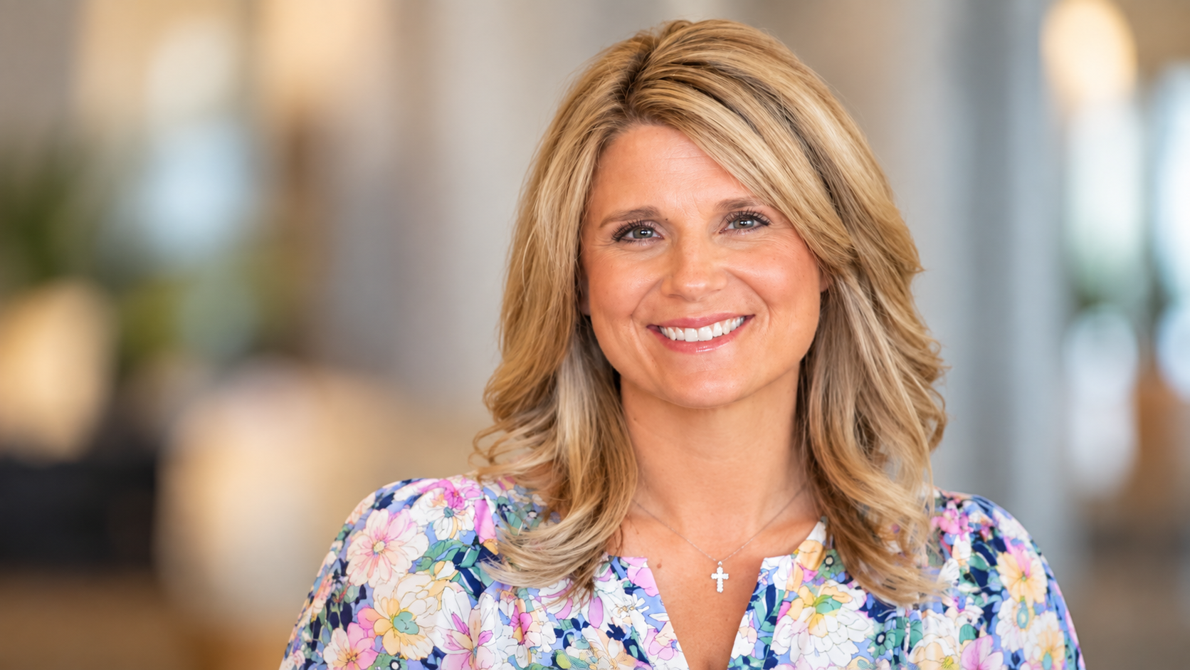 headshot of Childers wearing a floral shirt with a blurred background behind her