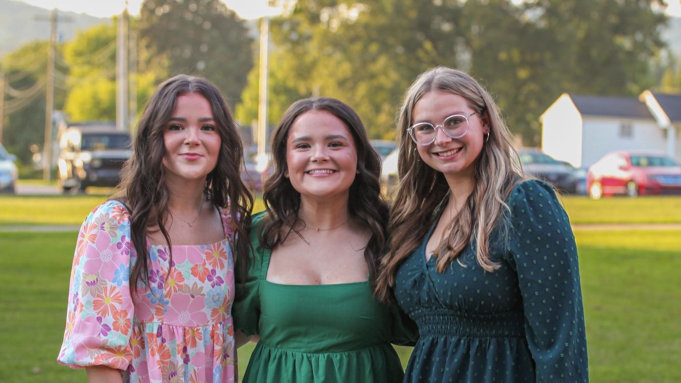 Three female Union Commonwealth University students are posing for a photo in the evening outside the Conway Boatman Chapel. They are standing together, arms around each other, all smiling and dressed in formal attire.